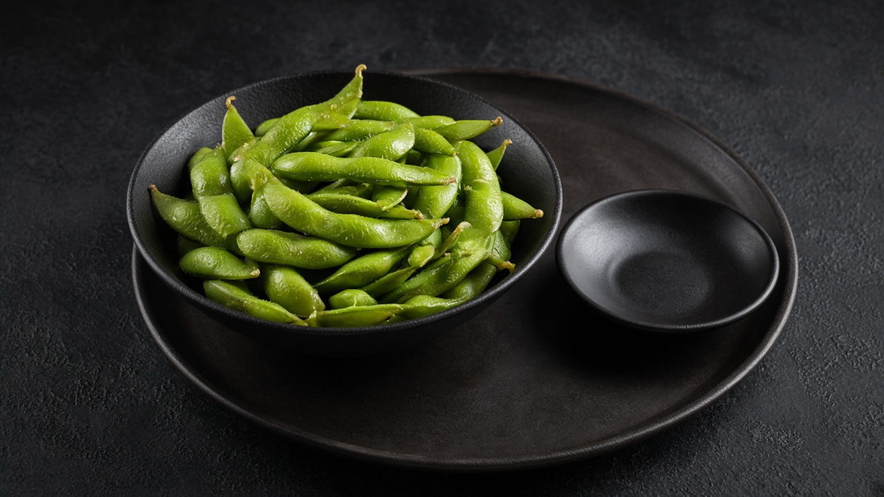 A bowl of bright green salted edamame pods with a small dish for empty shells.